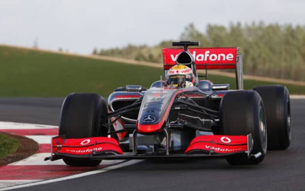 A MacLaren F1 car races on a track with green hills in the background, 2K Desktop Wallpaper