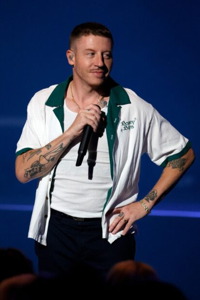 Macklemore is holding a microphone during a live performance with tattoos visible on his arms, HD Phone Wallpaper