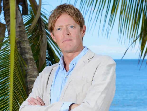 A serious man stands in front of palm trees and the ocean in Death In Paradise Tv Series, 2K Desktop Wallpaper