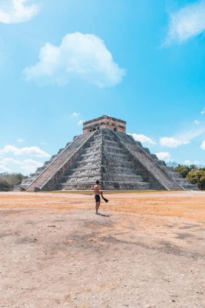 A man stands in front of the majestic Chichen Itza pyramid under a blue sky, HD Mobile Wallpaper