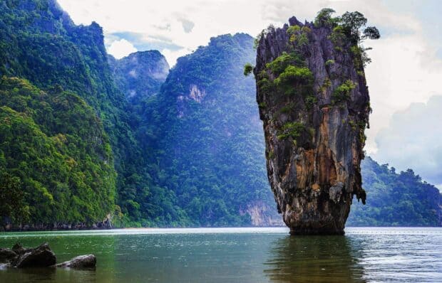 A stunning limestone cliff rises from the water in Phuket with lush green mountains in the background, HD Desktop Wallpaper