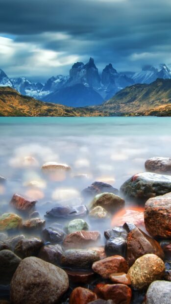 A serene lake with rocky foreground and towering mountains at Torres Del Paine National Park, HD Mobile Wallpaper