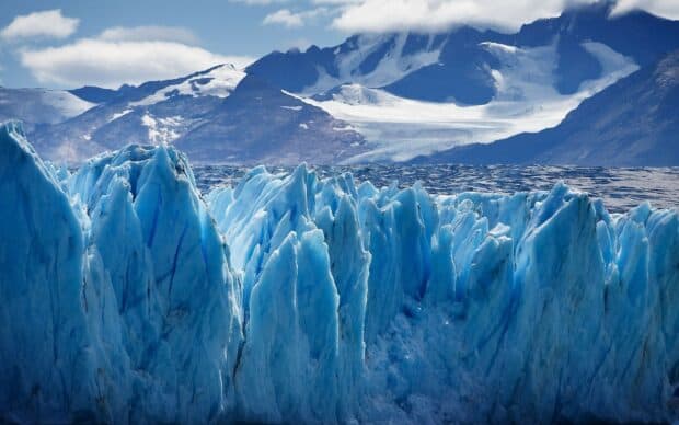The glacier displays stunning blue ice formations beneath snowy mountain peaks, 2K Desktop Wallpaper