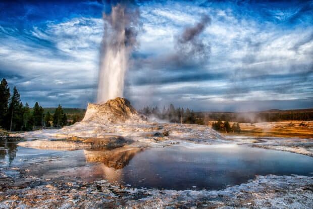 A geyser erupts dramatically with steam rising over Yellowstone National Park landscape, HD Desktop Wallpaper