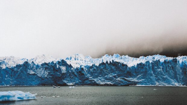 A majestic glacier rises above cold water under a cloudy sky, 4K Desktop Wallpaper
