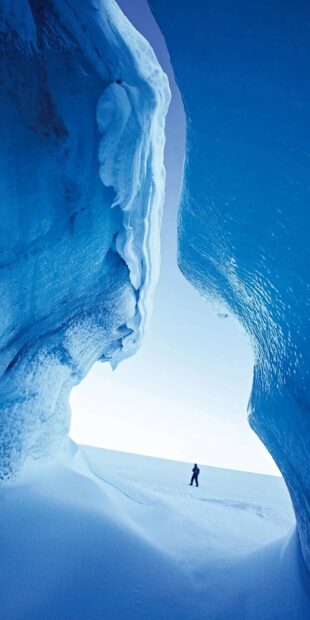 A lone explorer walks through a majestic glacier landscape covered in deep blue ice, HD Phone Wallpaper