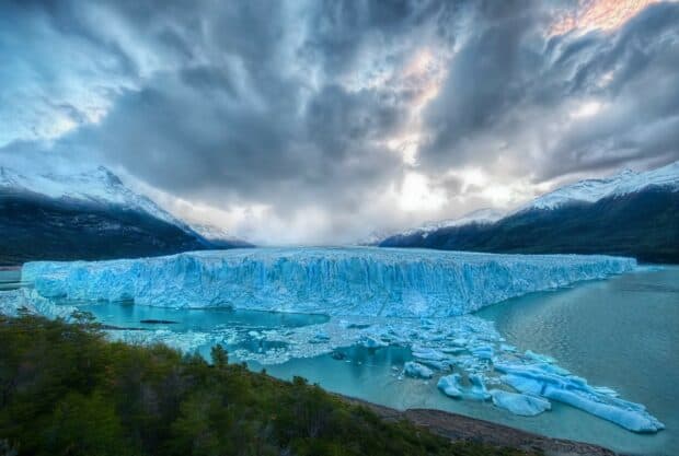 A large glacier surrounded by mountains and water with a cloudy sky above, HD Desktop Wallpaper