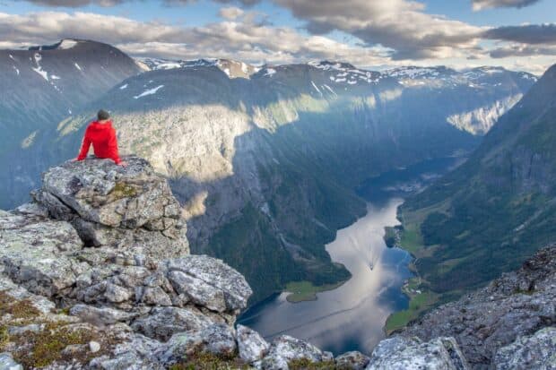A person in a red jacket overlooks the deep Norwegian fjords surrounded by rocky mountains, HD Desktop Wallpaper