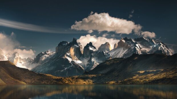 The snow capped peaks of Torres Del Paine National Park rise above the calm lake under a cloudy sky, HD Desktop Wallpaper