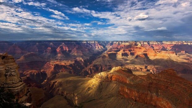 The Grand Canyon shows vast rock formations under a blue sky with clouds, HD Desktop Wallpaper