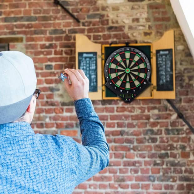 A man is focused on throwing a dart at a dartboard mounted on a brick wall, HD Desktop Wallpaper