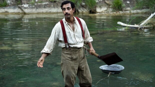 A man wearing suspenders and old fashioned clothes pans for gold in a shallow river, 4K Desktop Wallpaper