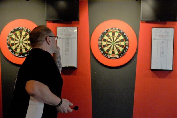 A man is focused on throwing a dart at a dartboard during a game, HD Desktop Wallpaper