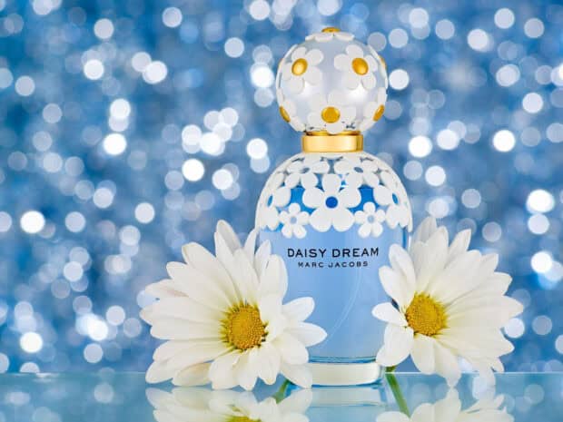 A Marc Jacobs Daisy Dream perfume bottle surrounded by white daisies on a blue bokeh background, HD Desktop Wallpaper