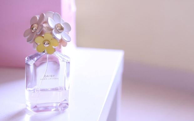 A clear Marc Jacobs Daisy perfume bottle with colorful flower decorations on a white surface, 2K Desktop Wallpaper
