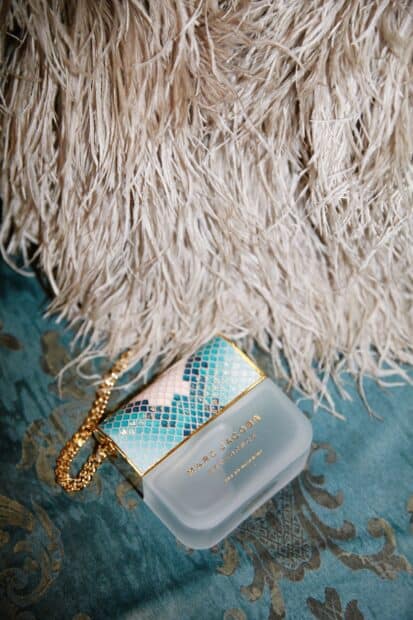 A Marc Jacobs perfume bottle lies on a blue textured fabric alongside beige fringed material, HD Phone Wallpaper