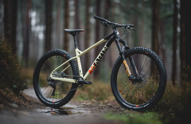 A Marin Bikes mountain bike stands on a muddy forest trail with tall trees in the background, HD Desktop Wallpaper