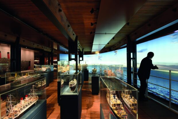 A person observes detailed ship models inside a maritime museum exhibit, HD Desktop Wallpaper