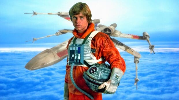 Mark Hamill in pilot suit holding helmet with spacecraft in background, 2K Desktop Wallpaper