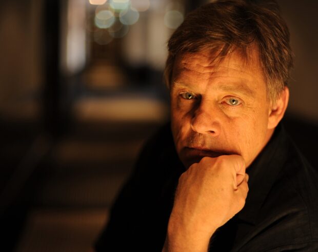 Mark Hamill is shown with a contemplative expression in warm lighting, HD Desktop Wallpaper