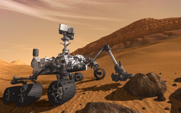 The Mars Curiosity Rover is captured exploring rocky terrain on Mars under a cloudy sky, HD Desktop Wallpaper