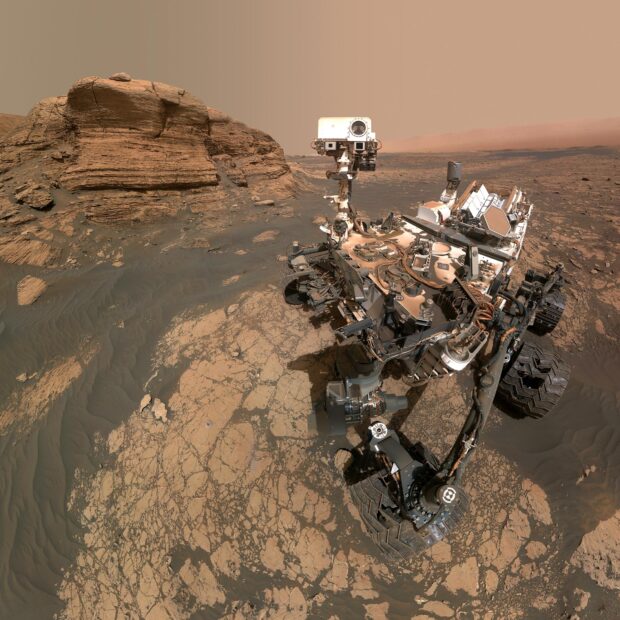 The Mars Curiosity Rover is captured navigating the rocky Martian surface with geological formations in the background, HD Desktop Wallpaper