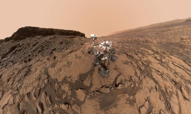 The Mars Curiosity Rover is captured navigating the rocky and dusty surface under a hazy orange sky, 2K Desktop Wallpaper