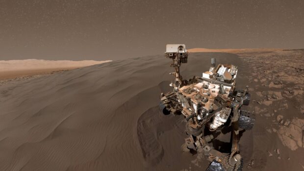 The Mars Curiosity rover is captured moving across sand dunes under a starry sky, 4K Desktop Wallpaper