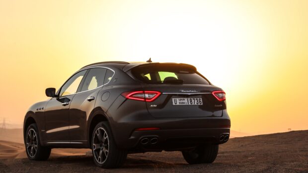 A Maserati Levante SUV is parked on desert sand with the sun setting behind it, 4K Desktop Wallpaper