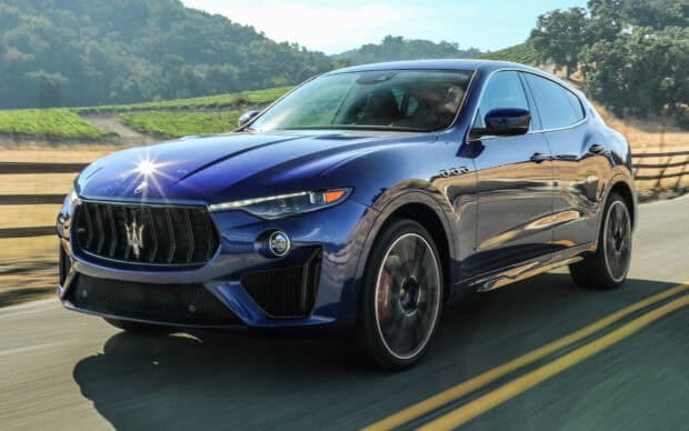 A blue Maserati Levante is driving on a sunny mountain road with greenery in the background, HD Desktop Wallpaper