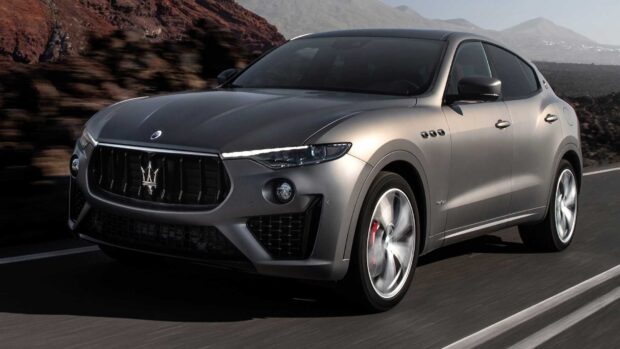 A silver Maserati Levante drives swiftly on a mountainous road under clear skies, HD Desktop Wallpaper