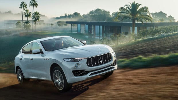A white Maserati Levante drives fast on a dirt road near a modern house with palm trees, 4K Desktop Wallpaper