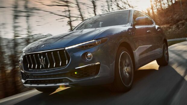A Maserati Levante is driving quickly along a curved forest road with sunlight reflecting off its surface, HD Desktop Wallpaper
