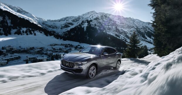 A Maserati Levante drives swiftly on a snowy mountain road with sun shining brightly above, 2K Desktop Wallpaper