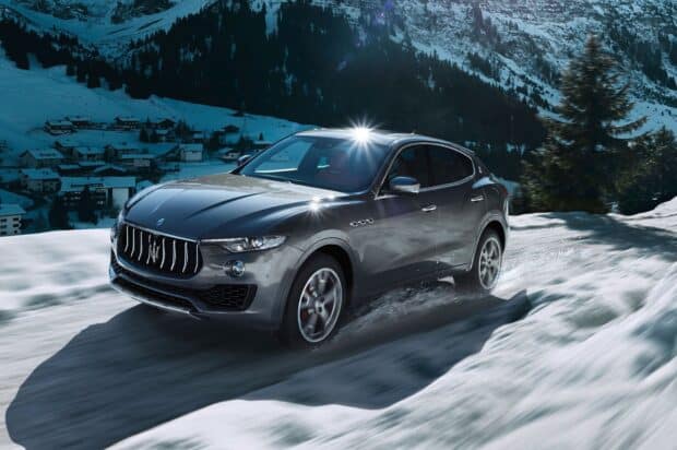 A Maserati Levante is driving through a snowy mountain landscape with trees and houses in the background, HD Desktop Wallpaper