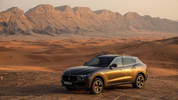 A Maserati Levante is parked on sandy terrain with desert mountains in the background, 4K Desktop Wallpaper
