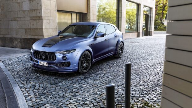 A blue Maserati Levante is parked on a cobblestone street near modern buildings, 4K Desktop Wallpaper
