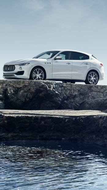 A white Maserati Levante is parked on a rocky ledge above the water under a clear sky, HD Mobile Wallpaper