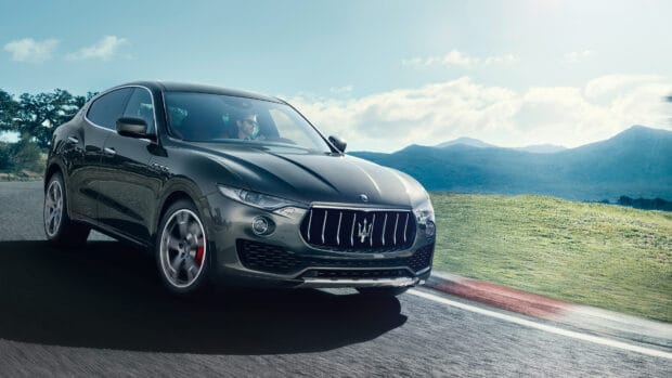 A Maserati Levante is shown driving fast on a curvy mountain road with clear skies, 4K Desktop Wallpaper