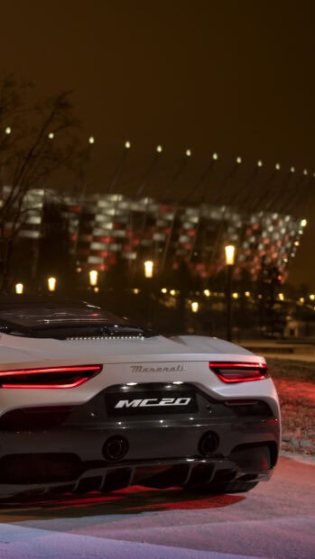 A white Maserati MC20 is parked with illuminated taillights and a blurry lit building in the background, 4K Phone Wallpaper
