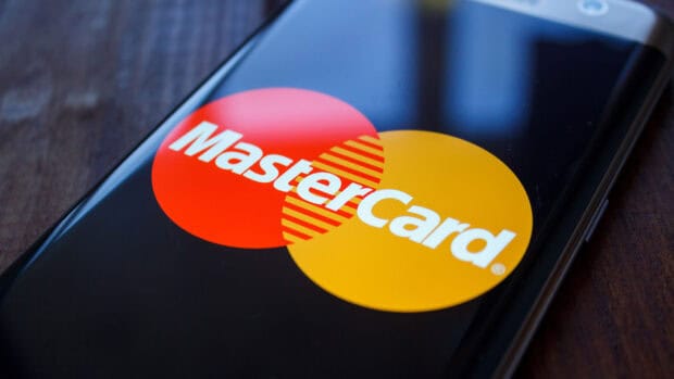 The image shows Mastercard logos displayed on a smartphone screen resting on a wooden surface, HD Mobile Wallpaper