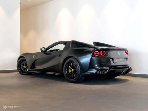 A matte black Ferrari 812 Gts is parked indoors showing the rear and side design, HD Desktop Wallpaper