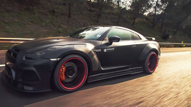 A matte black Nissan GT R with custom rims is driving on a forest road during daylight, HD Desktop Wallpaper