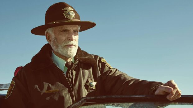 A mature sheriff wearing a brown uniform and hat stands beside a vehicle under a clear sky in Fargo Wallpapers, 2K Desktop Wallpaper