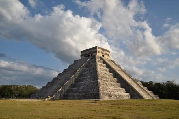 The Mayan pyramid at Chichen Itza stands under a cloudy sky with surrounding greenery, 2K Desktop Wallpaper