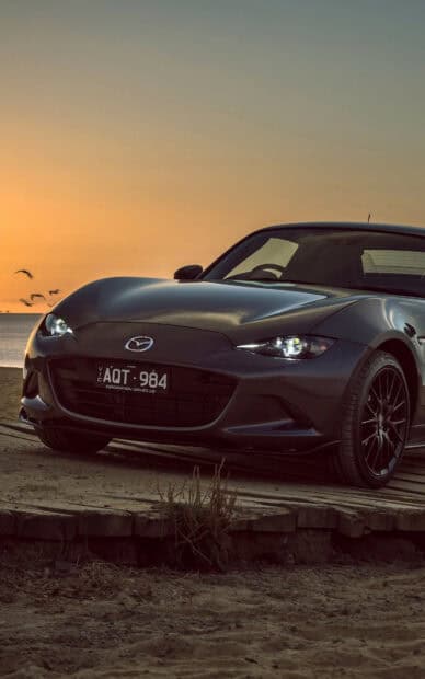 A Mazda MX 5 Miata is parked near the beach during a sunset with birds flying in the background, HD Phone Wallpaper