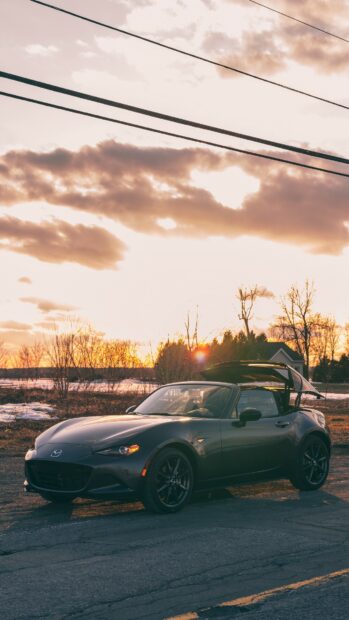 A Mazda MX 5 Miata is parked with its roof opening during sunset on a rural road, HD Phone Wallpaper