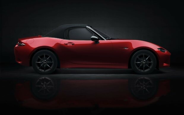 A red Mazda MX 5 Miata convertible car with a black soft top is displayed from the side in a dark studio, 2K Desktop Wallpaper