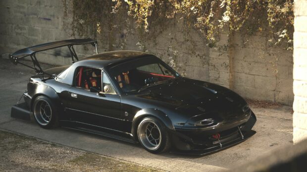 A black Mazda Mx 5 Miata with racing modifications parked by a textured wall, 4K Desktop Wallpaper