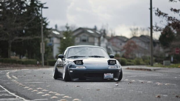 A lowered Mazda MX 5 Miata is parked on an empty street with houses in the background, 4K Desktop Wallpaper